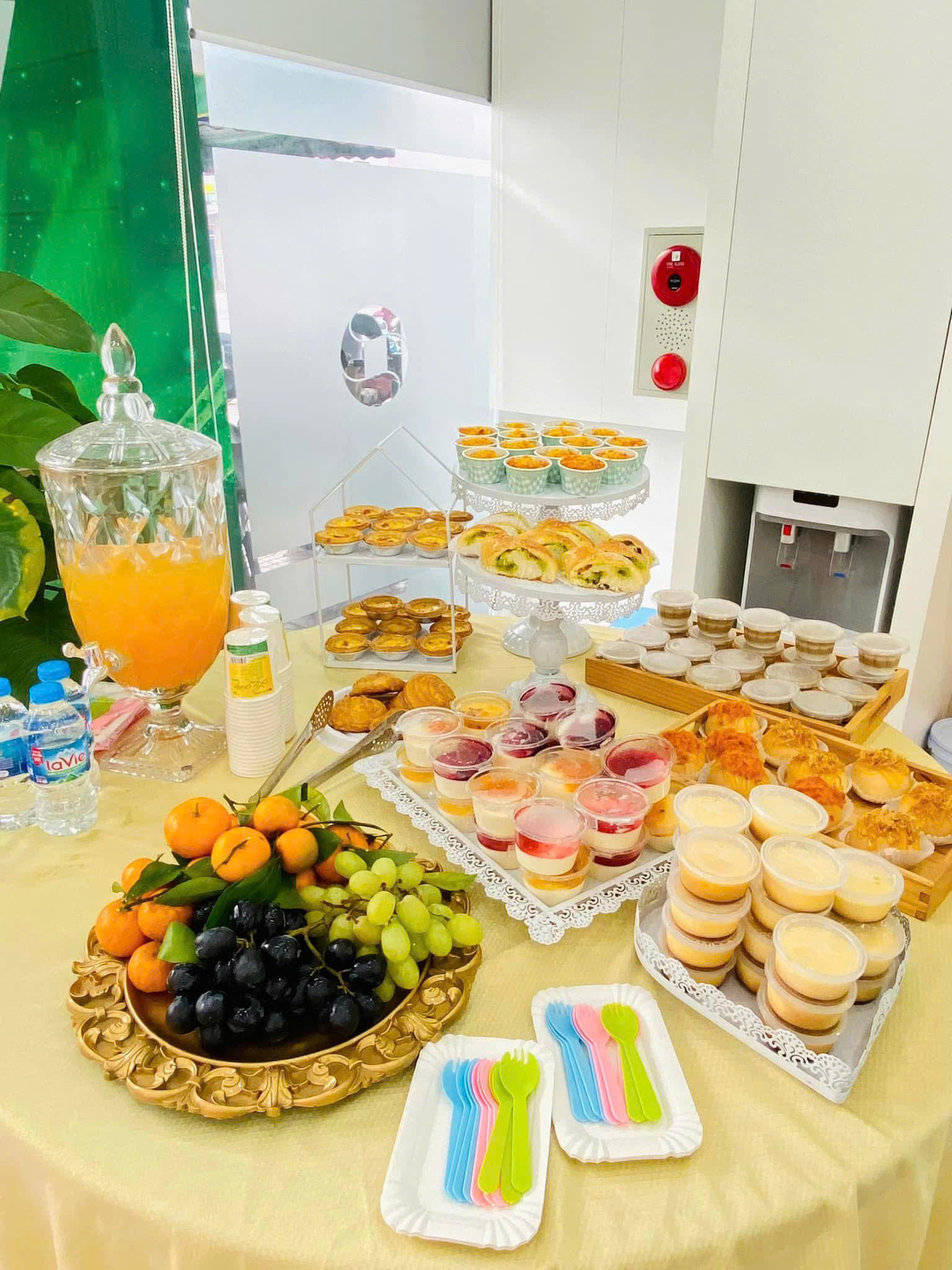 Bàn tea break văn phòng với bánh, trái cây, pudding và nước uống